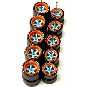 May include: A collection of miniature black tires with orange rims and light blue star-shaped wheel centers. Each tire has a silver pin through the center. The tires are stacked in pairs, with the Goodyear Eagle logo visible on the sidewalls.
