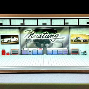May include: A diorama display case with a white interior and a brown frame. The case features a variety of classic Ford Mustang models, including a black Mustang with the word "Mustang" in white letters on the front. The case also includes a variety of accessories, such as tools and a toolbox.
