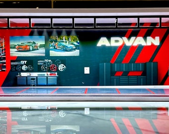 May include: A miniature model of a garage with a red and black striped wall featuring the word "ADVAN" in white. The garage has a glass front and a black tiled floor. There are two small cars and a set of tires on display inside the garage.