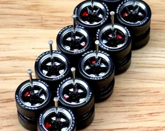 May include: A collection of miniature black Goodyear Eagle tires with silver rims and red brake details. Each tire has a silver pin inserted in the center. The tires are stacked on a light brown wooden surface.
