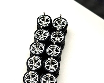 May include: A collection of miniature black tires with silver rims, each featuring the text "TOYO" and "PROXES STW". The wheels are stacked and arranged on a white surface, with a corner of a black and white patterned box in the background.