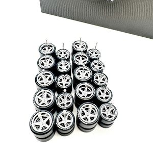 May include: A collection of miniature black rubber tires with silver five-spoke rims, each featuring a central metal pin. The tires have white Goodyear lettering on the sidewalls. A black box with the text SHOP164 is visible in the background.
