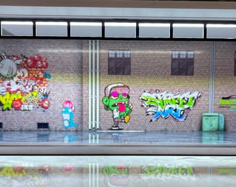 May include: A miniature diorama of a brick building with graffiti art. The building has a garage door and windows. The graffiti art includes a cartoon character, a car, and various colourful designs.