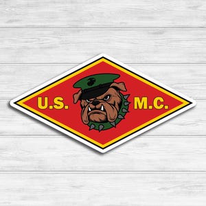 May include: A red diamond-shaped sticker with a yellow border. The sticker features a cartoon bulldog wearing a green military hat with a gold emblem. The text "U.S. M.C." is printed in yellow letters on the sticker.