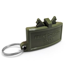 May include: A green plastic keychain shaped like a grenade with the text "FRONT TOWARDS ENEMY" printed on it.
