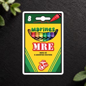 May include: A rectangular sticker featuring a yellow box design with the text Marines MRE Menu 69 8 Assorted Crayons. The graphic includes a row of eight colorful crayons, a red crayon icon, and a red Marine Corps emblem at the bottom.