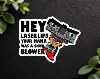 May include: A die-cut sticker featuring a gray robot with large blue eyes and orange accents, wearing a red bandana. The text reads: HEY LASER LIPS YOUR MAMA WAS A SNOW BLOWER. The design has a white border and is set against a dark textured background.