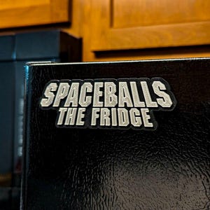 May include: A black refrigerator with a silver sticker that says "Spaceballs The Fridge".