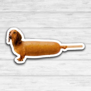 May include: A brown dachshund dog is depicted as a corn dog. The dog's body is a long, golden brown corn dog, and the dog's head and legs are visible. The dog is standing on a white surface.