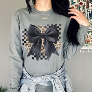 May include: A gray long-sleeved sweatshirt with a black and white checkered pattern and a large black bow with a leopard print design.