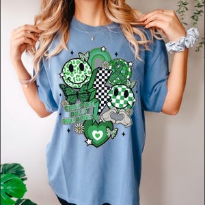 May include: A light blue t-shirt with a green, white and black graphic design. The design features a smiley face, a lightning bolt, a heart, and the text "Cerebral Palsy Awareness".