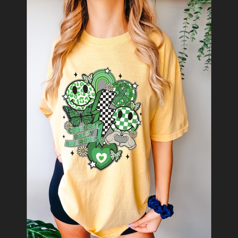 May include: A yellow t-shirt with a green, black and white graphic design featuring smiley faces, butterflies and the text "Cerebral Palsy Awareness".