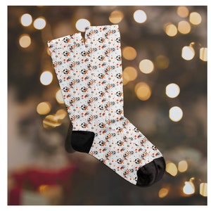 May include: A pair of white socks with a black and orange soccer ball pattern. The socks have a black cuff.