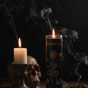 An Oyin Beauty Essentials Ancestor Candle burning alongside a smaller ritual candle with rising smoke, symbolizing ancestral connection, wisdom, and sacred energy.