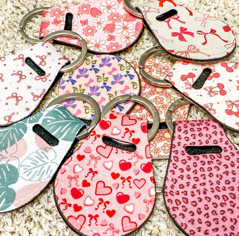 K&ouml;nnte beinhalten: Eine Sammlung bunter Schl&uuml;sselanh&auml;nger mit verschiedenen Mustern, darunter Herzen, Blumen und geometrische Designs. Die Schl&uuml;sselanh&auml;nger sind aus Stoff gefertigt und haben einen Metallring zum Anbringen von Schl&uuml;sseln.