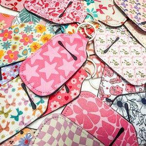 May include: A collection of colorful fabric keychains with various patterns, including floral, geometric, and star designs. Each keychain features a metal ring and a black fabric trim.