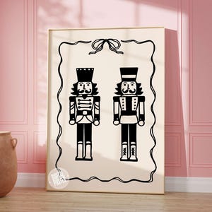 May include: Black and white printable art print featuring two nutcracker soldiers with a bow at the top. The print has a white background and a black border.