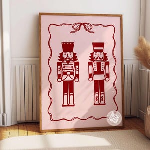 May include: A digital poster featuring two red nutcracker soldiers on a pink background with a decorative border. The nutcrackers are standing side by side and have a whimsical, festive look.