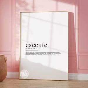 Puede incluir: Un póster blanco con marco dorado que presenta la palabra "execute" en texto negro. La definición de la palabra se proporciona en texto negro más pequeño debajo. El póster está en una pared rosa.