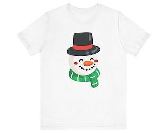 May include: White t-shirt with a cartoon snowman wearing a black top hat with a red band and a green scarf.