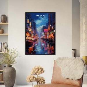 May include: A framed print of a painting depicting a nighttime scene in Osaka, Japan. The painting shows a canal with buildings and streetlights on either side. The water is reflecting the lights and there are people walking along the canal.
