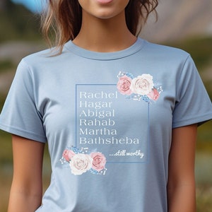 May include: Light blue t-shirt with a floral design and the text "Rachel, Hagar, Abigal, Rahab, Martha, Bathsheba...still worthy".