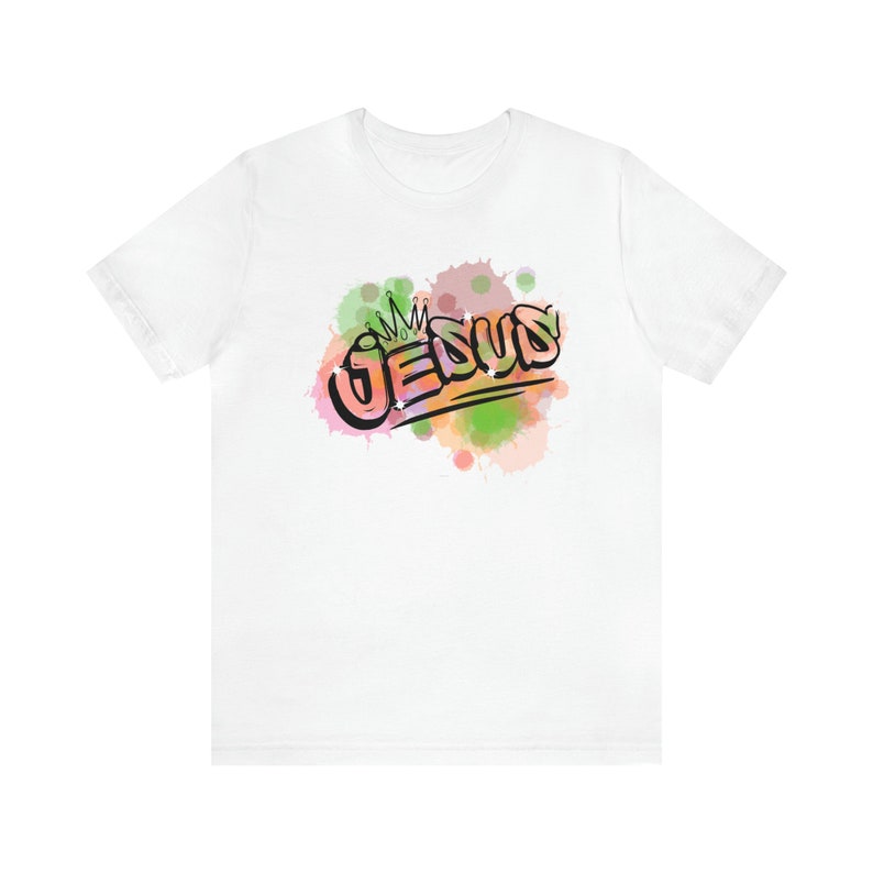 May include: White t-shirt with a colorful watercolor design of the word "JESUS" with a crown above it.
