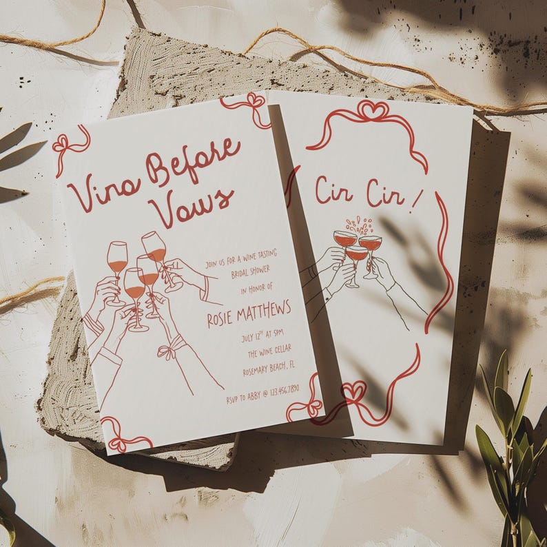 May include: Two white cards with red text and illustrations. One card reads "Vino Before Vows" and the other "Cir Cir!". Both cards feature line drawings of hands toasting wine glasses. The cards are for a bridal shower.