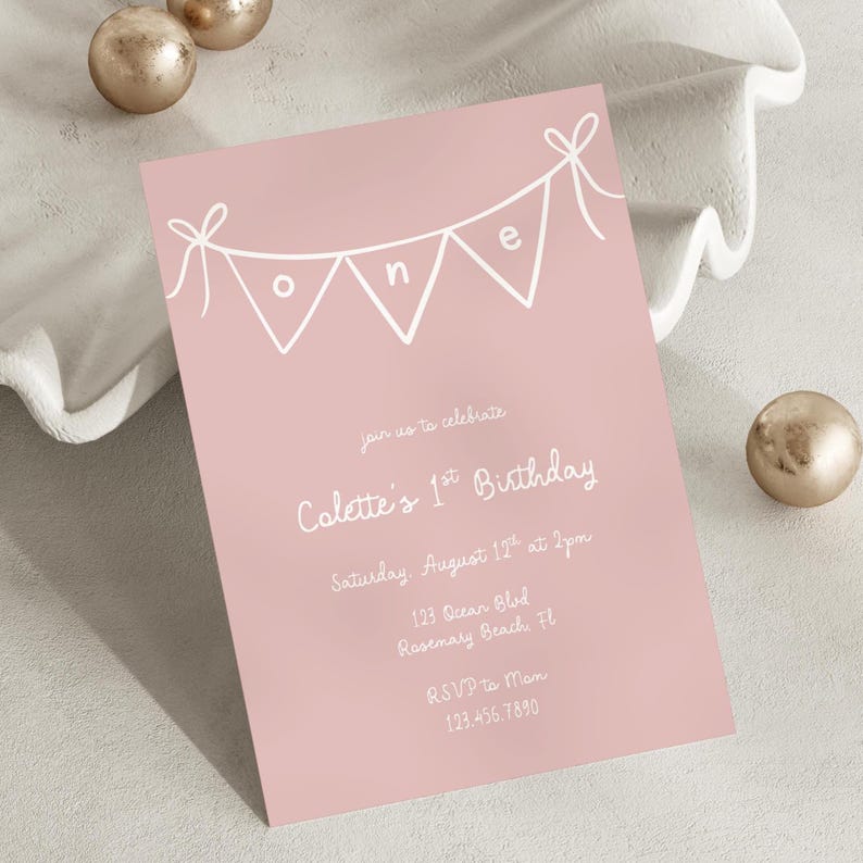 May include: A pale pink birthday invitation with white text and a banner design spelling "one". The invitation is for Colette's 1st birthday, including the date, time, location, and RSVP details. The card is rectangular.