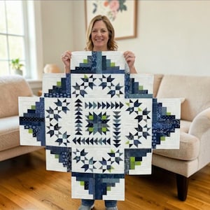 May include: A handmade quilt with a geometric design. The quilt features a central square with star and triangle patterns in shades of blue, green, and white. The quilt is held up in front of a person.