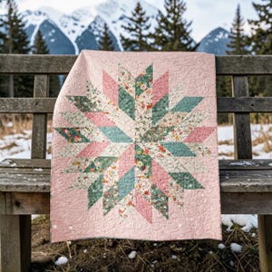 Puede incluir: Un edredón hecho a mano con un diseño de estrella, con secciones alternas de tela rosa, verde azulado y con estampado floral. El edredón se exhibe en un banco de madera con un telón de fondo de montaña nevada. Dimensiones: 152 cm x 152 cm.