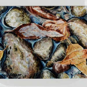 May include: Watercolour painting of autumn leaves in a stream. The leaves are shades of brown, orange, and yellow, and they are floating on top of the water. The water is a dark blue colour, and there are some rocks in the stream.