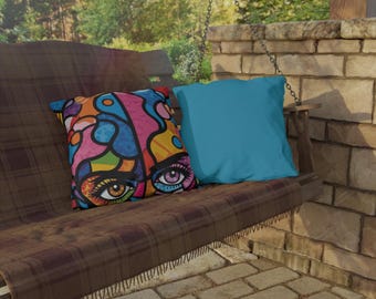 Pode incluir: Um balanço de xadrez marrom com duas almofadas. Uma almofada é azul e a outra tem um design abstrato colorido com um olho grande.