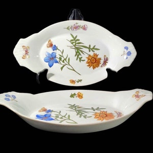 May include: Two white oval serving platters with floral and butterfly designs. The platters feature blue, orange, and purple flowers with green stems and leaves. Butterflies are also depicted. The platters have scalloped edges.