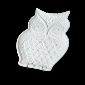 May include: White ceramic owl-shaped dish with a textured surface and raised eyes. The dish has two metal hooks on the bottom.