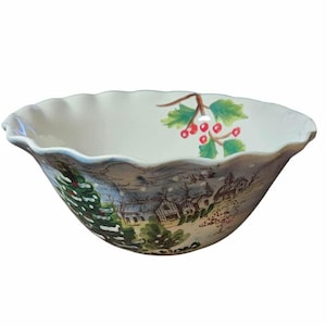 May include: A white ceramic bowl with a scalloped rim features a winter scene with a snowy village, evergreen trees, and red berries.