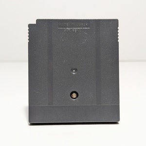 Op de afbeelding: Een zwarte Game Boy Color-spelcartridge met de tekst "MADE IN JAPAN" en "PAT. PEND." gedrukt op de achterkant.