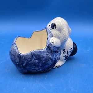 May include: Blue and white ceramic planter shaped like a rabbit. The rabbit is sitting on its haunches with its head tilted back. The planter has a crackled glaze and a floral design.