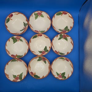 May include: A set of nine round ceramic bowls arranged in a three-by-three grid. Each bowl features a cream-colored interior and a hand-painted design of brown branches with green leaves and small reddish-purple fruit accents along the inner rim.