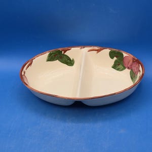 May include: An oval-shaped ceramic serving dish with a cream-colored interior and a central divider. The rim features a brown painted edge, and the interior is decorated with hand-painted green leaves and reddish-pink fruit motifs on both sides.