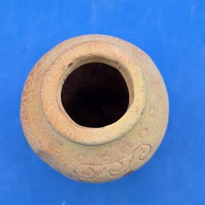 An overhead view of the light brown terracotta vase, showing the circular opening of its narrow neck and etched tribal patterns on the rim.
