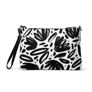 May include: A rectangular clutch bag with a black and white floral pattern. The design features bold, abstract black flower shapes and leaf-like forms on a white background. It has a black wrist strap and a zip closure.