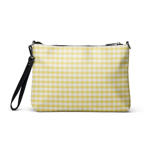 May include: A rectangular clutch bag with a yellow and white gingham pattern, a black wrist strap and a black zipper. The bag is a light yellow colour with a white grid pattern. The wrist strap is black.