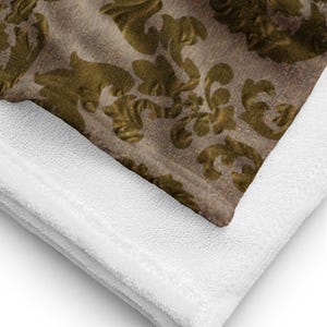 May include: A folded blanket featuring a detailed gold and brown floral pattern. The blanket is layered over a white, textured fabric, creating a contrast in colour and texture. The design is ornate and classic.