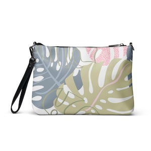 May include: A rectangular clutch bag with a black wrist strap and zip closure. The bag features a botanical design with large, stylised leaves in shades of grey, green, pink, and white. The overall design is modern and stylish.