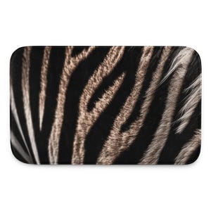 May include: Rectangular bath mat featuring a zebra print pattern. The design showcases alternating black and brown stripes with a textured appearance, mimicking the natural look of zebra fur. The mat has rounded corners.