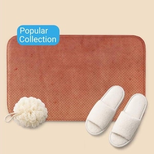 Puede incluir: Un juego de baño con una alfombra de baño rectangular de color marrón rojizo, dos zapatillas blancas de punta abierta y una esponja vegetal de color crema. El rectángulo azul en la esquina superior izquierda dice "Popular Collection".