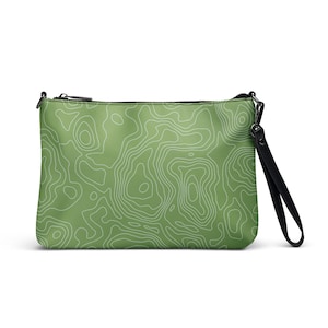 May include: A green clutch bag featuring a white topographic map design. The bag has a black zip closure and a black wrist strap. The rectangular bag is made of a smooth material.