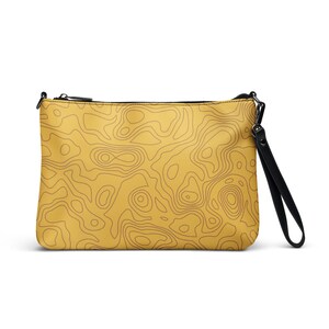 May include: Mustard yellow clutch bag featuring a brown topographic map design. The bag has a black zip, a black wrist strap, and black hardware. The rectangular bag appears to be made of a durable material.