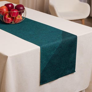 May include: A teal table runner on a white tablecloth. A gold wire basket filled with red apples sits on the table. A white chair is in the background.